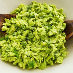 chopped green goddess salad being tossed in a large white bowl in a large white serving bowl