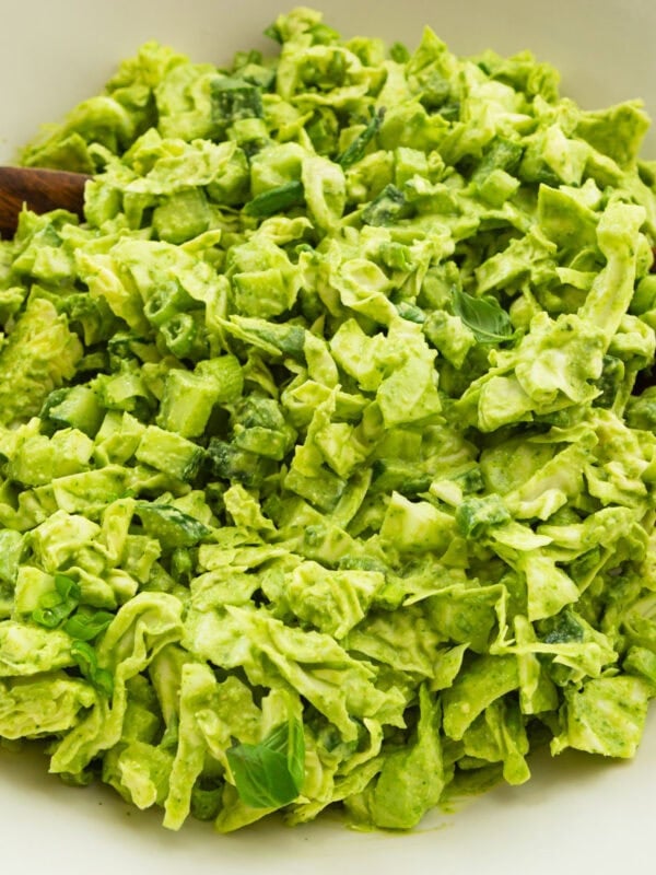 chopped green goddess salad being tossed in a large white bowl in a large white serving bowl