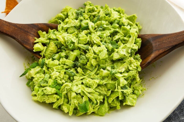 chopped green goddess salad being tossed in a large white bowl in a large white serving bowl