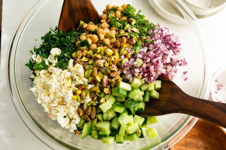 all the ingredients for a viral jennifer aniston salad being stirred together with wooden salad tongs