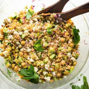 a large glass bowl full of a chickpea, quinoa and cucumber salad with red onions and feta cheese