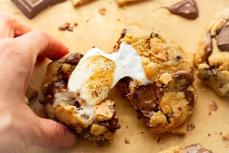 someone separating a s'more cookie showing the golden gooey marshmallow in a s'more cookie