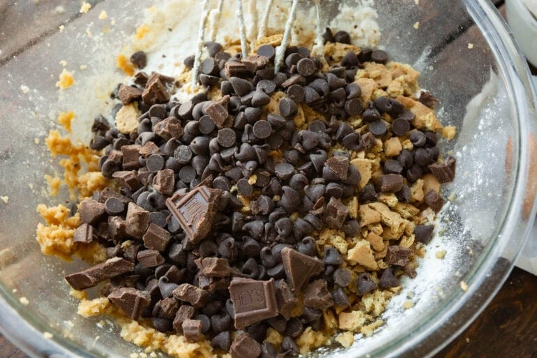 chunks of hershey's chocolate bar being stirred into s'more cookie dough