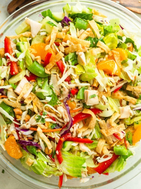 a large glass bowl full of wonton chicken salad with shredded cabbage, mandarin oranges. sliced red peppers and wonton strips