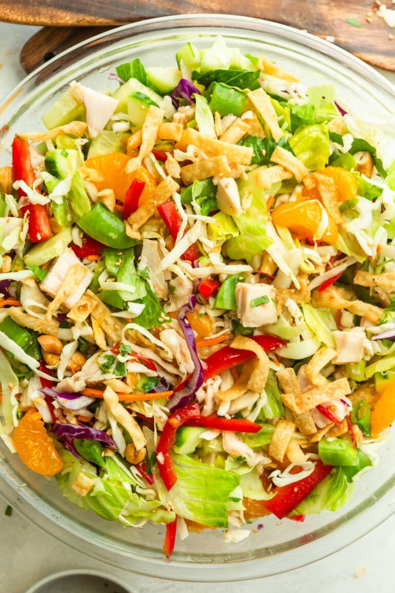 a large glass bowl full of wonton chicken salad with shredded cabbage, mandarin oranges. sliced red peppers and wonton strips