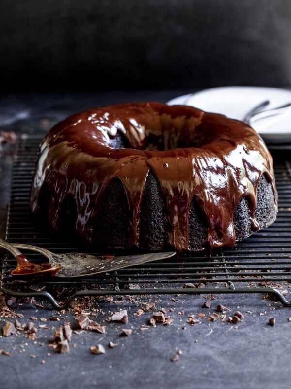 A zucchini chocolate bundt cake with a rich chocolate glaze. The cake is on a wire cooling rack and has mini chocolate chips scattered under and around the rack.